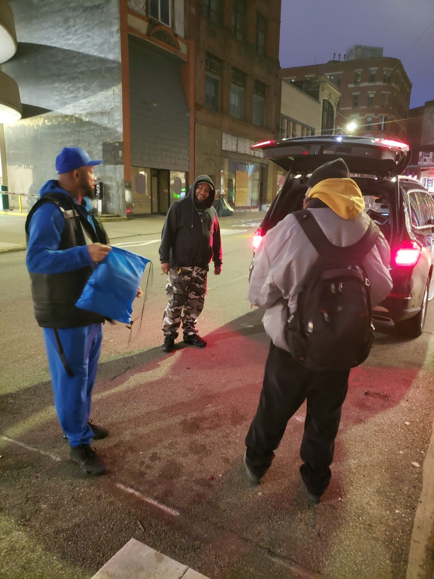 A volunteer hands a care package to a man downtown at night